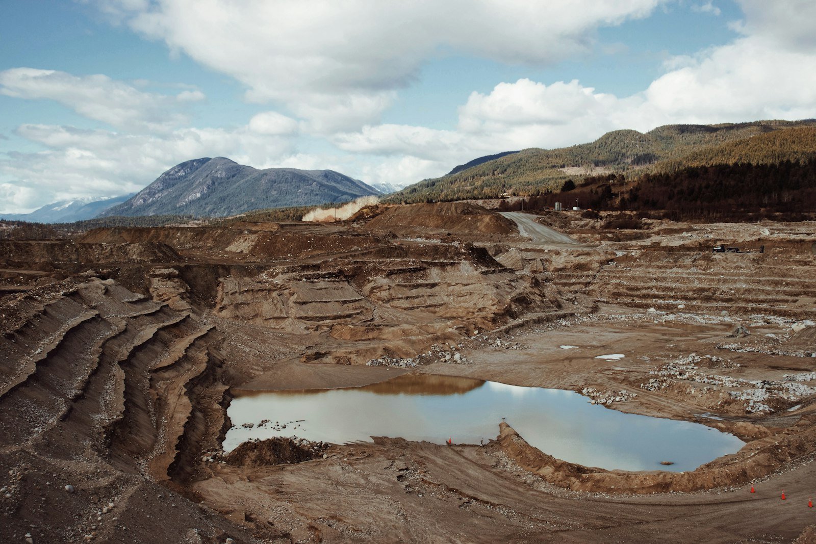 Terraced open-pit mine with water at its base and mountains beyond; illustrative mining landscape.